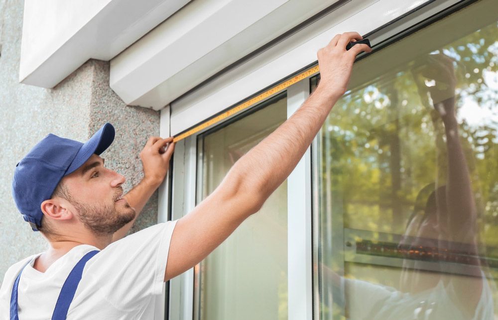 A Man is Measuring a Window With a Tape Measure — Budget Screens & Awnings in South Lismore, NSW