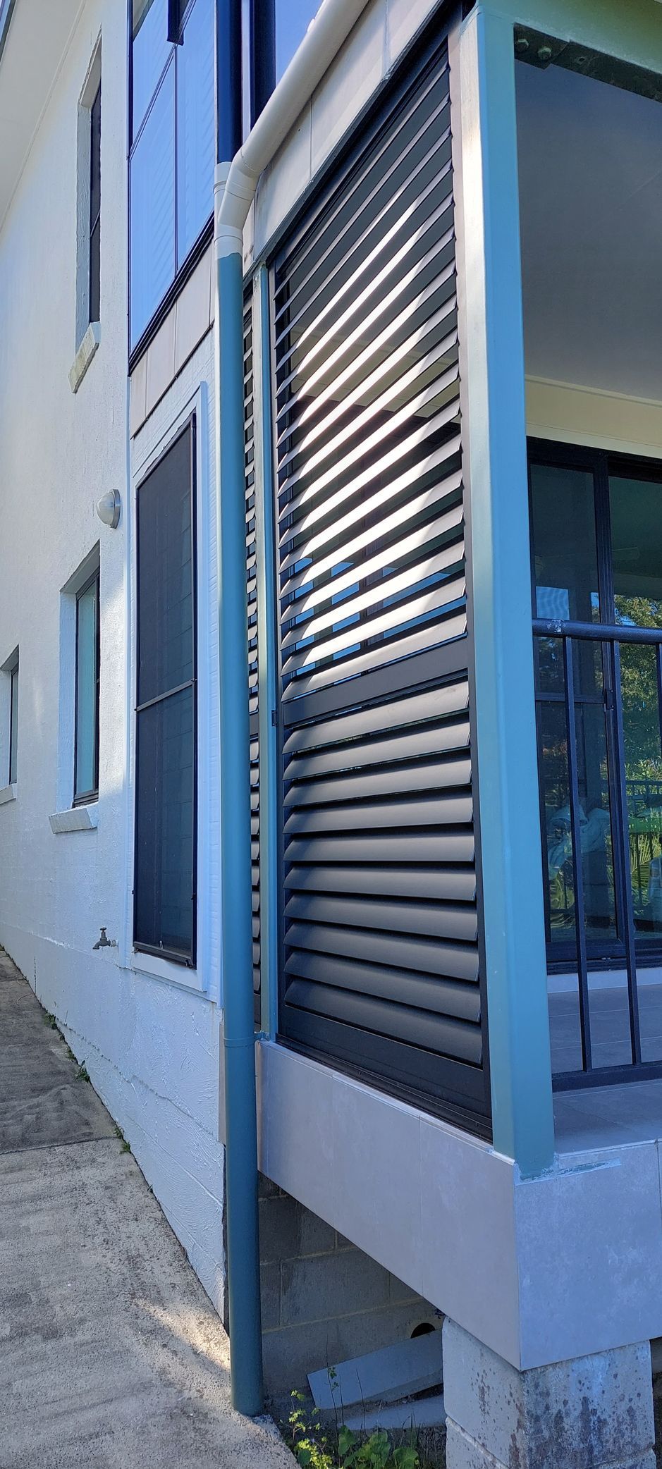 A white exterior wall with a downspout and dark window shutters — Budget Screens & Awnings in South Lismore, NSW