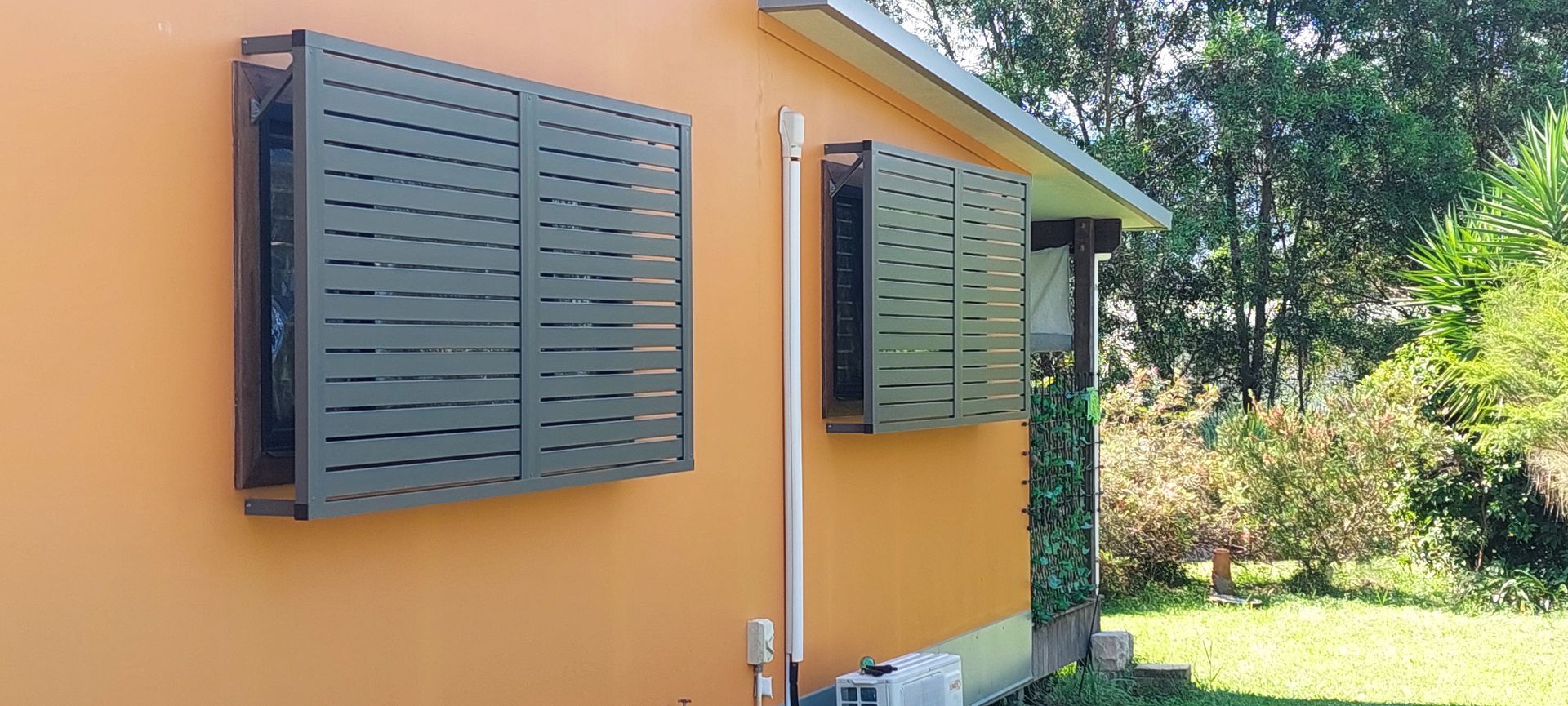 Two slatted window security shutters mounted on the exterior wall of a home — Budget Screens & Awnings in South Lismore, NSW