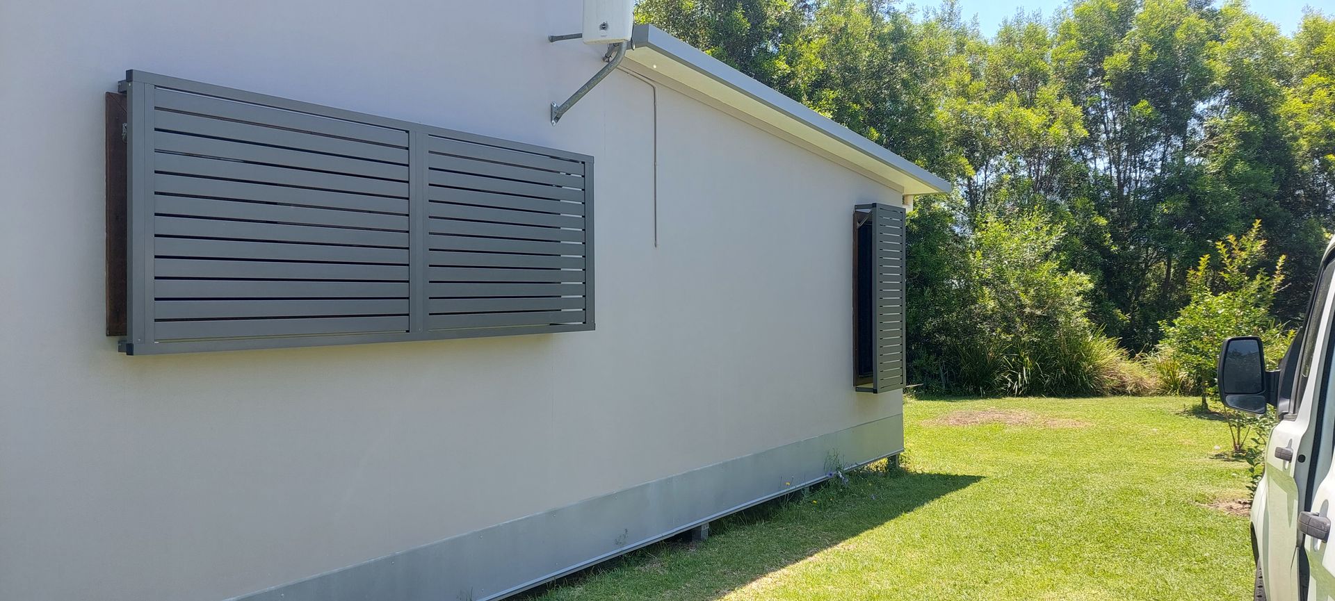 A house exterior features large, dark grey horizontal louvered shutters — Budget Screens & Awnings in South Lismore, NSW
