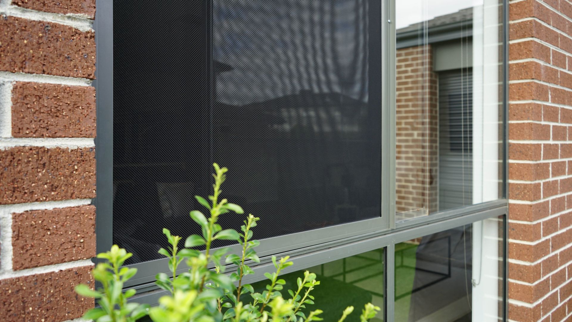 A black security screen fitted to a window on a red brick house — Budget Screens & Awnings in South Lismore, NSW