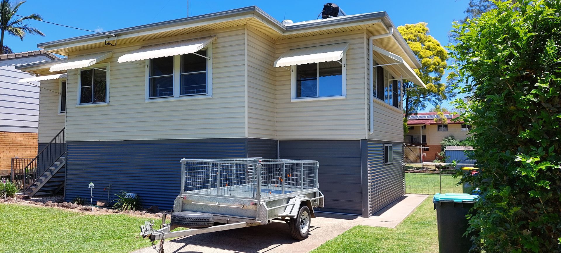 A light-yellow house with a dark grey base and white awnings — Budget Screens & Awnings in South Lismore, NSW
