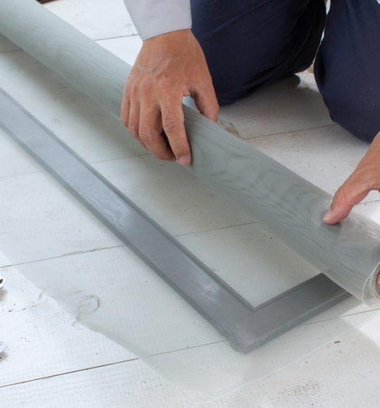 A Person is Kneeling on the Floor Holding a Window Screen — Budget Screens & Awnings in South Lismore, NSW
