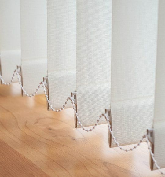 A Row of White Vertical Blinds on a Wooden Floor — Budget Screens & Awnings in South Lismore, NSW