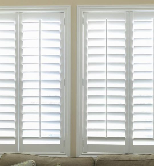 A Living Room With Two Windows With White Shutters and a Couch — Budget Screens & Awnings in South Lismore, NSW