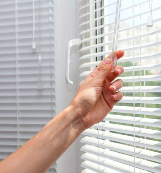 A Person is Opening a Window With Blinds on It — Budget Screens & Awnings in South Lismore, NSW
