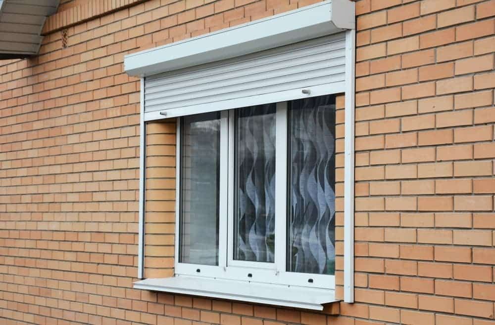 A Brick Building With a Window With a Roller Shutter on It — Budget Screens & Awnings in South Lismore, NSW
