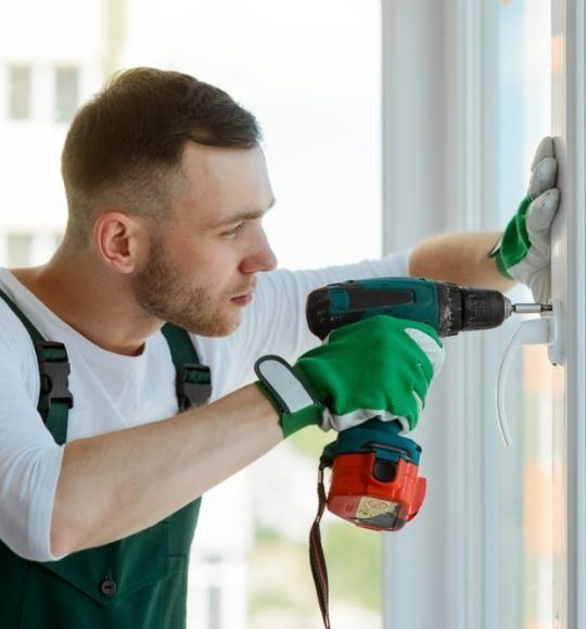 A Man is Using a Drill to Fix a Window — Budget Screens & Awnings in South Lismore, NSW