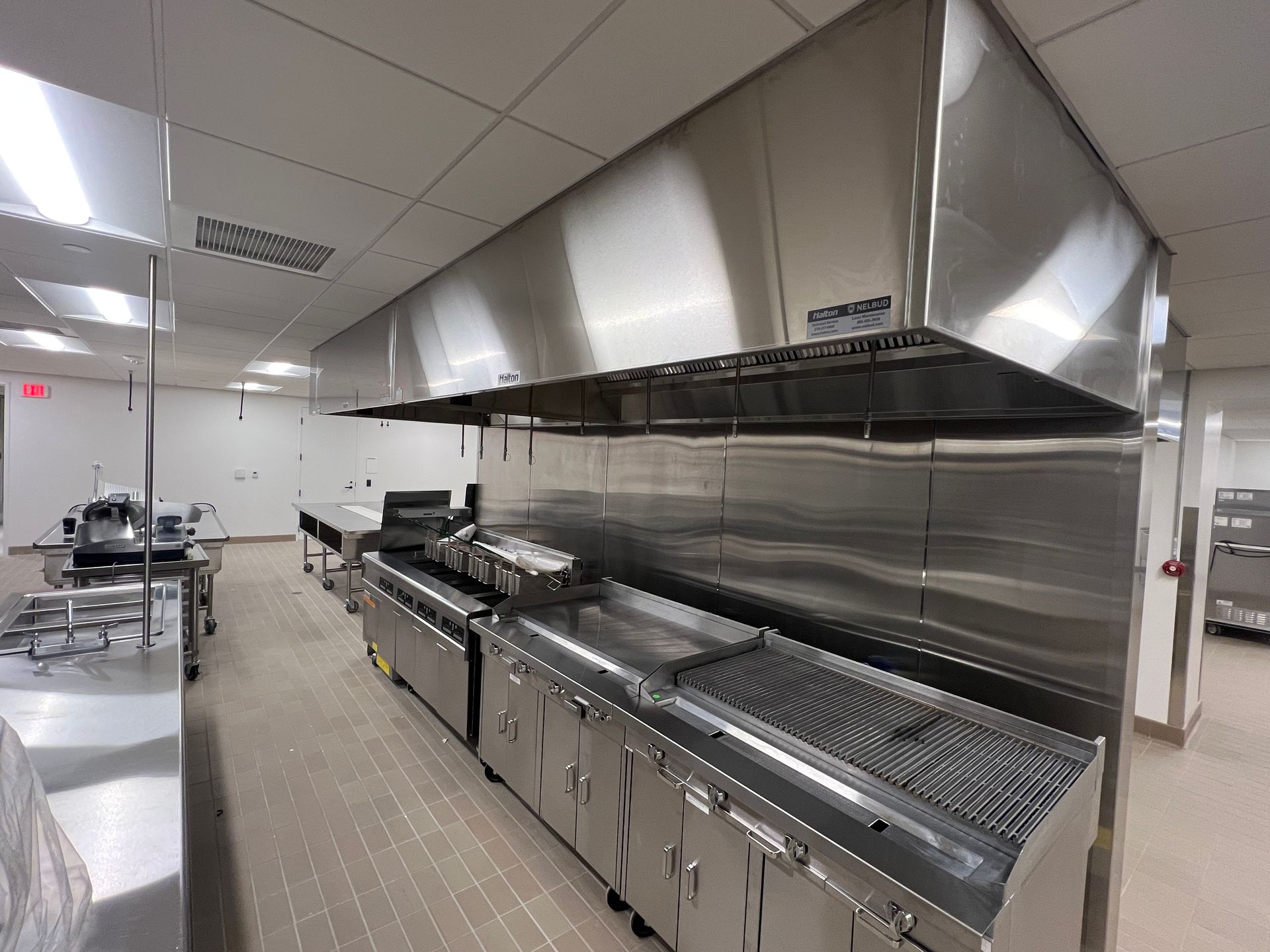 Commercial kitchen with stainless steel cooking line, large ventilation hood, and tiled floor