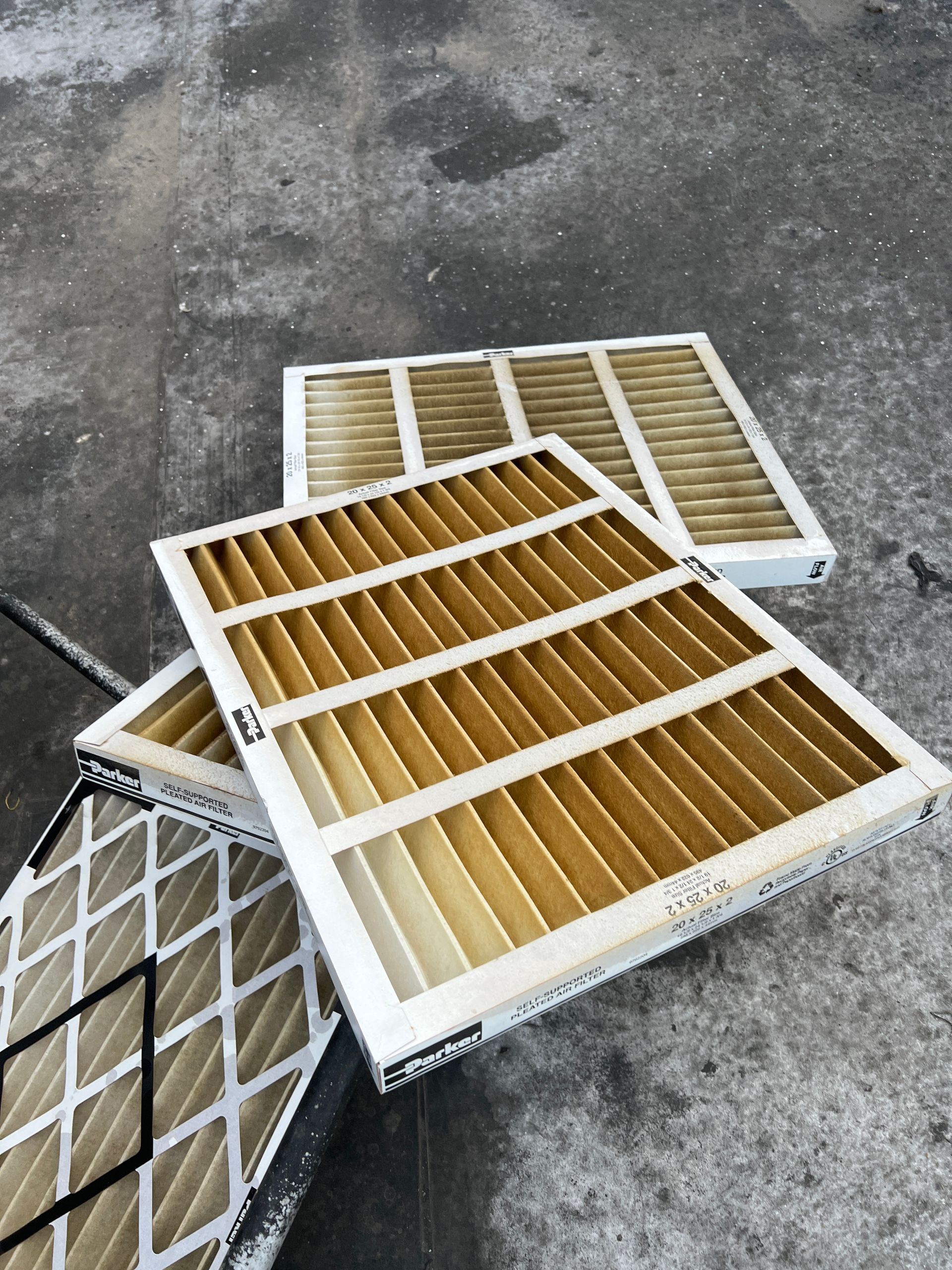 Three rectangular HVAC air filters with visible dust and debris, placed on a gray concrete surface.
