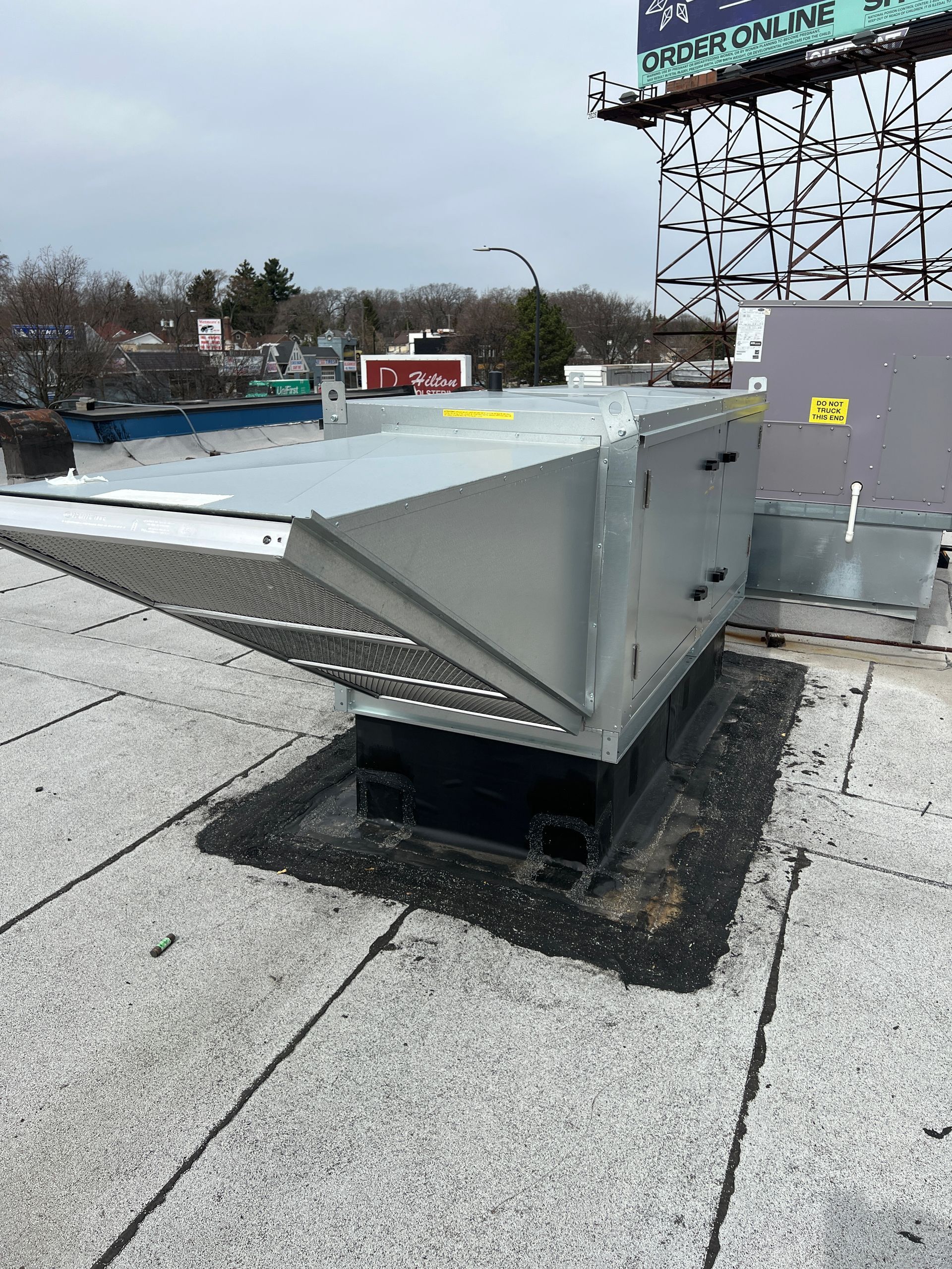 A gray industrial HVAC rooftop intake hood mounted on a flat, gravel-covered roof.