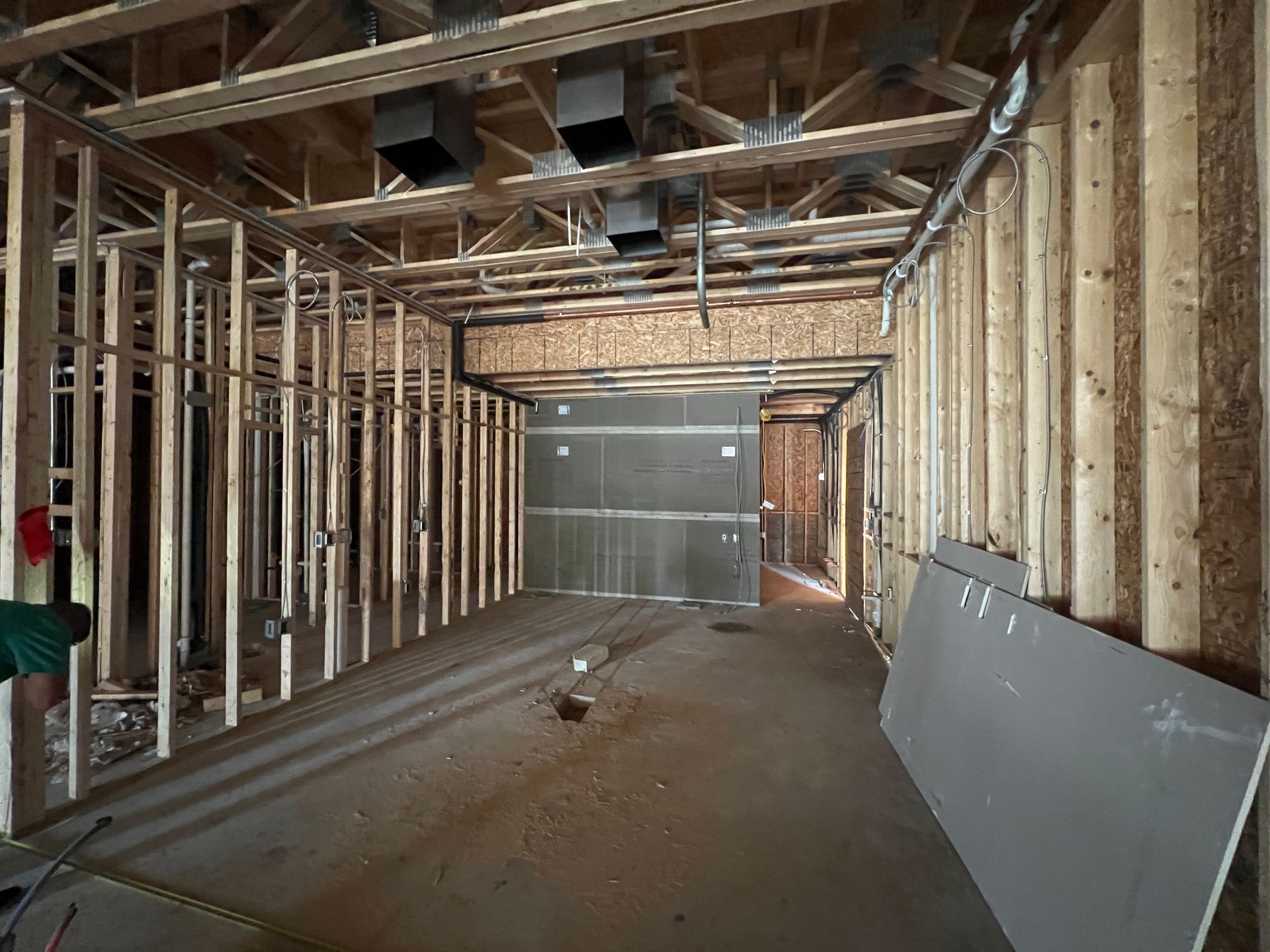Interior construction site showing wood-framed walls, exposed ceiling trusses, ductwork, and a partial drywall panel.
