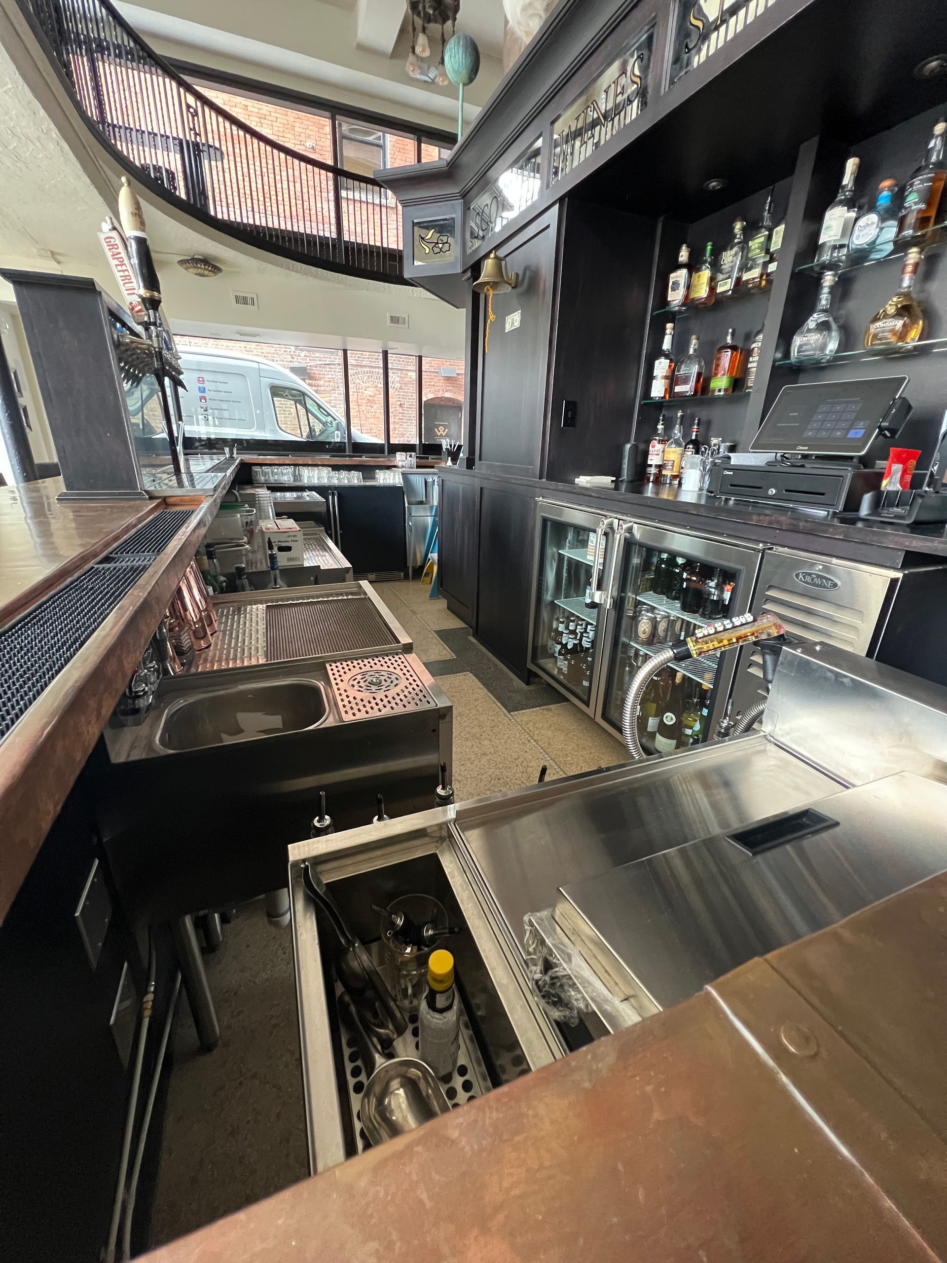 Modern bar interior with shelves of liquor, stainless counters, and a mirrored back wall