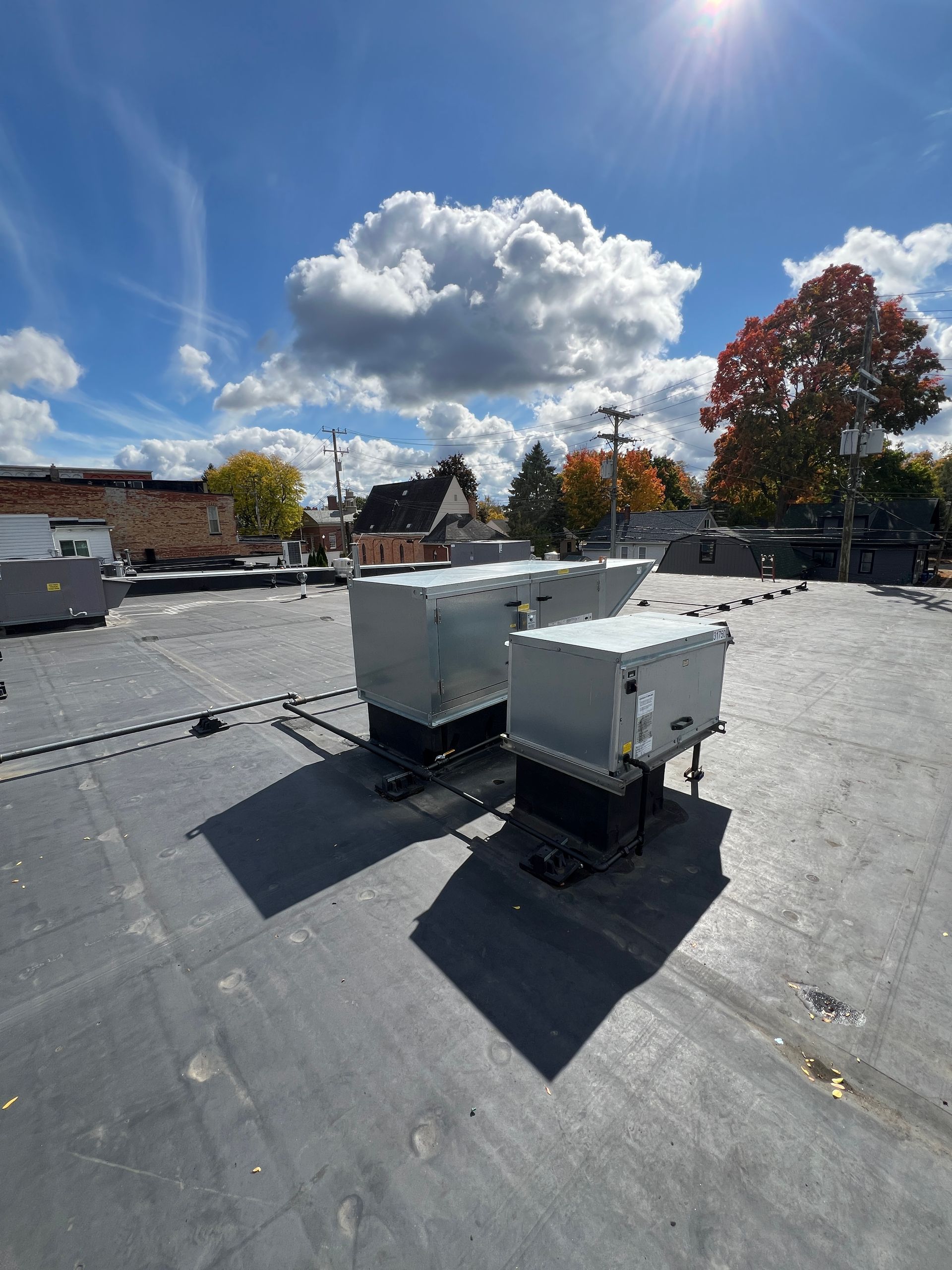HVAC units on a flat roof, sunny day, with a cloudy sky and trees in the background.