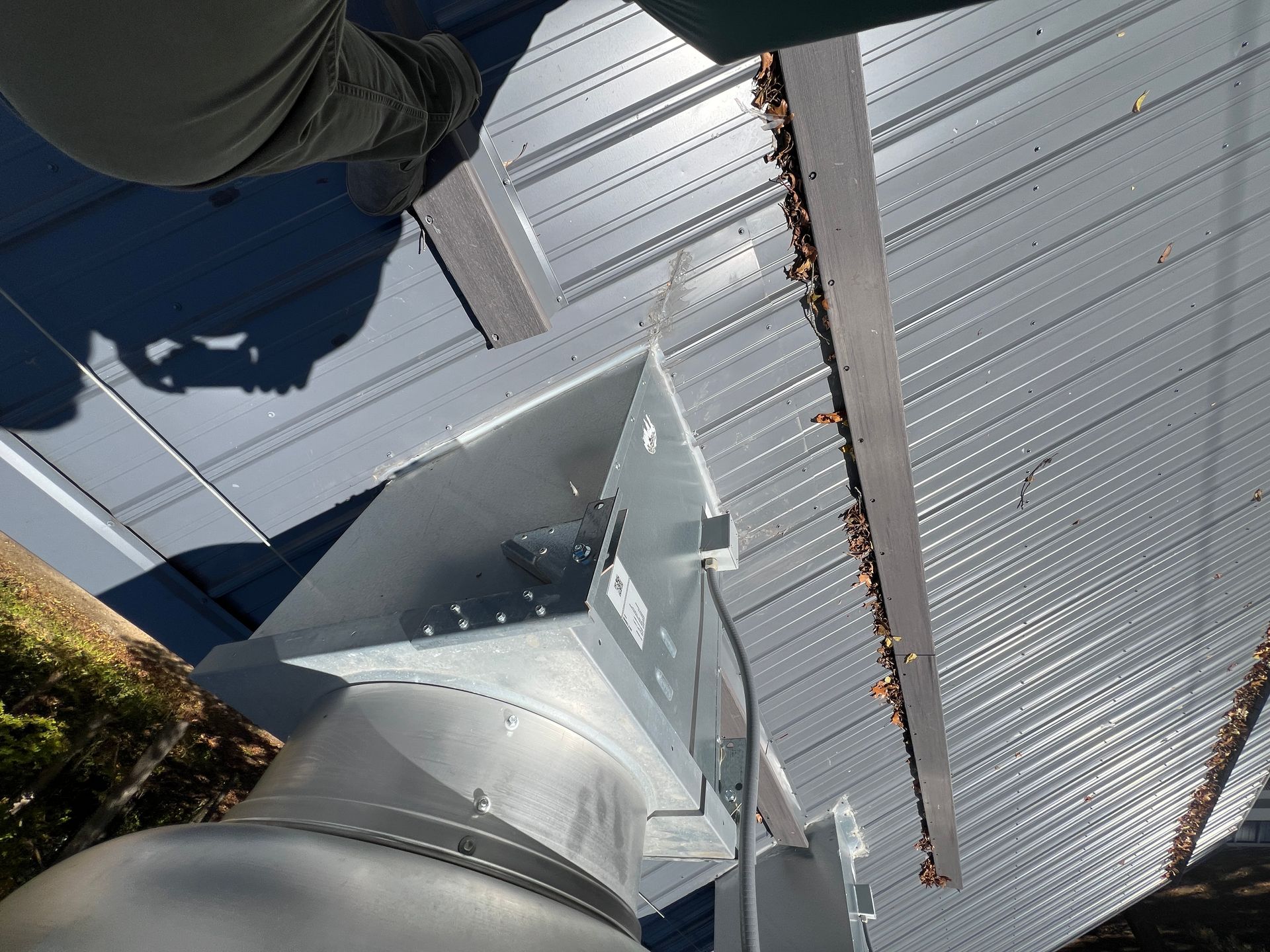 A person standing near a metal structure on a corrugated metal roof. The structure has a cylindrical base.