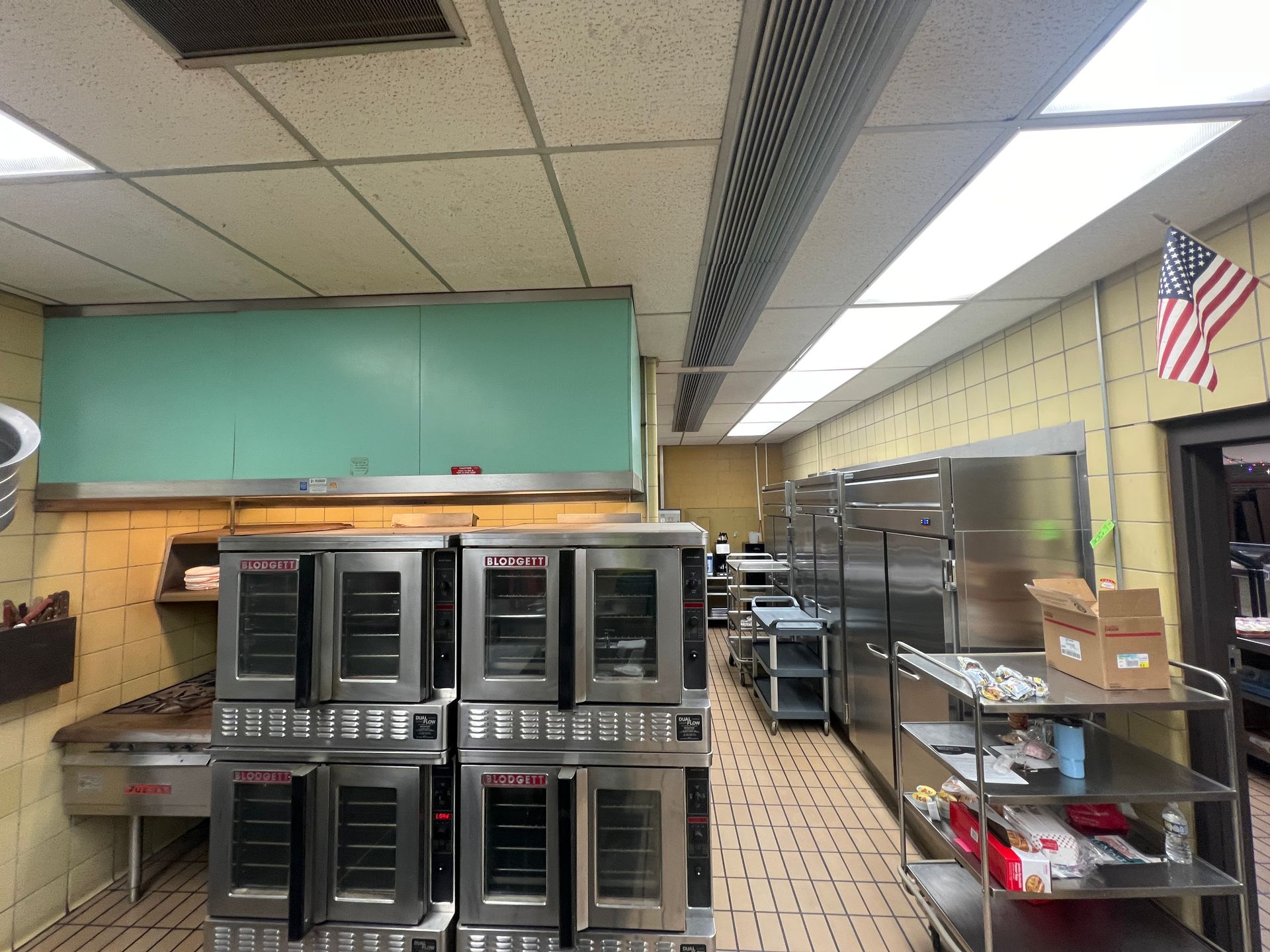 Commercial kitchen with ovens, stainless steel tables, and American flag.