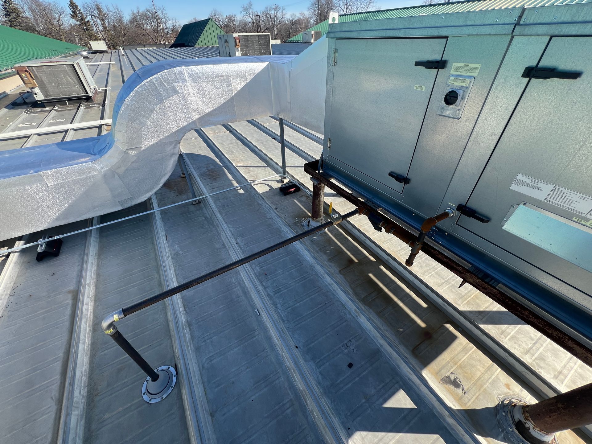 Rooftop with HVAC equipment, metal ductwork, and safety railing under a clear blue sky.