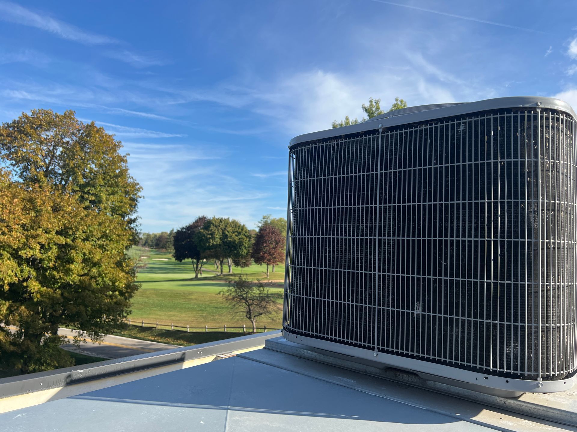 Large outdoor HVAC unit beside a parking lot with a grassy park and trees in the background