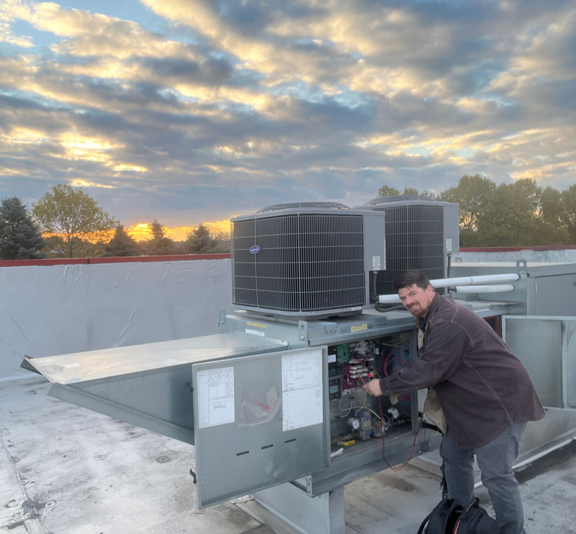 Technician servicing rooftop HVAC unit at sunset with cloudy sky in the background