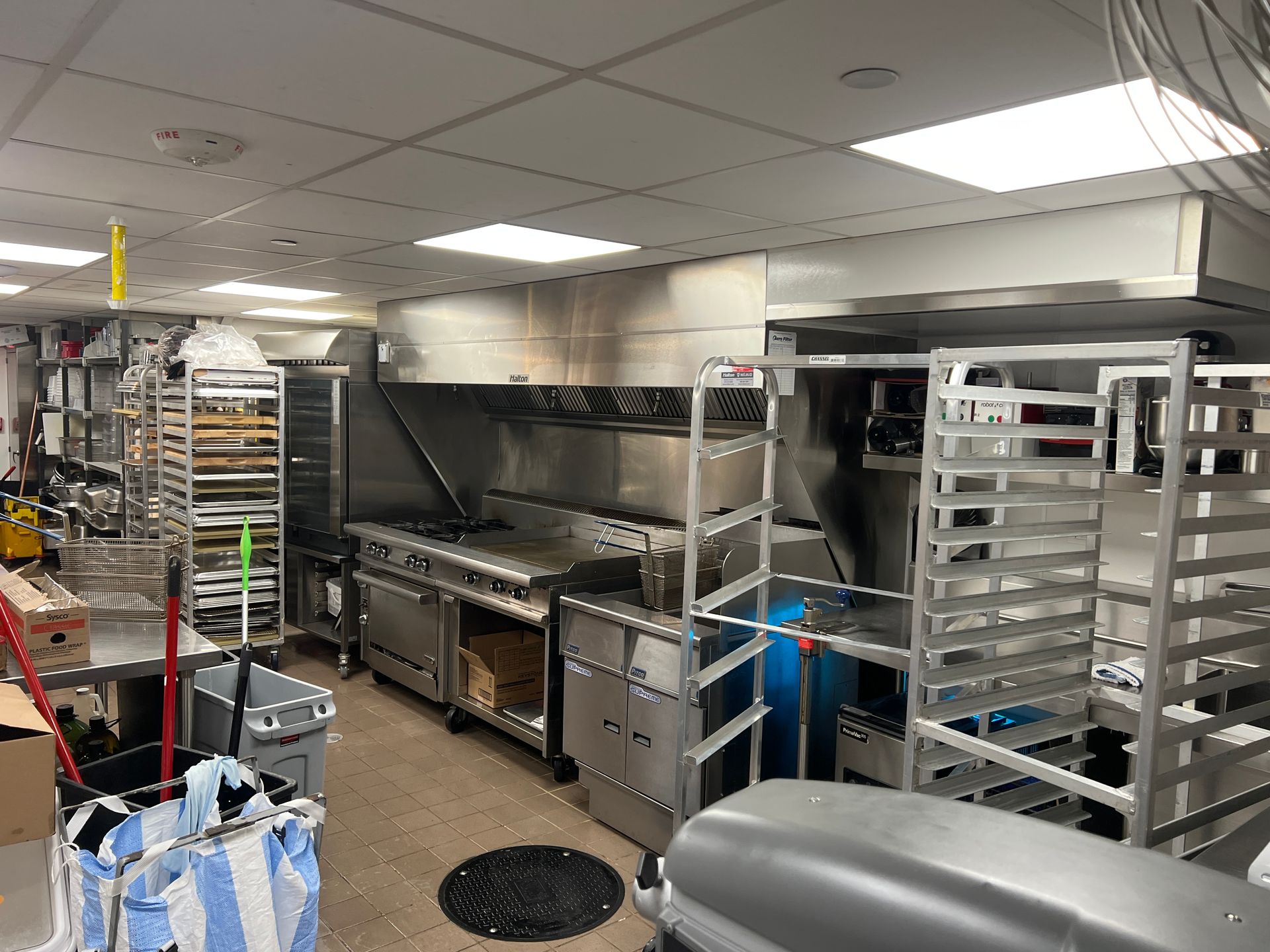 Commercial kitchen with stainless steel appliances, prep racks, and white tile ceiling