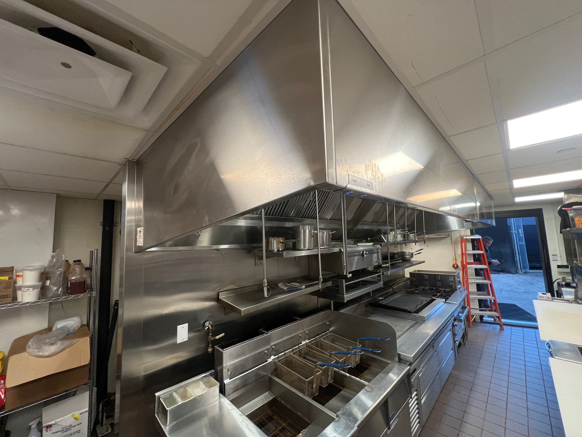 Commercial kitchen with stainless steel cooking line, ventilation hood, prep counters, and tiled floor