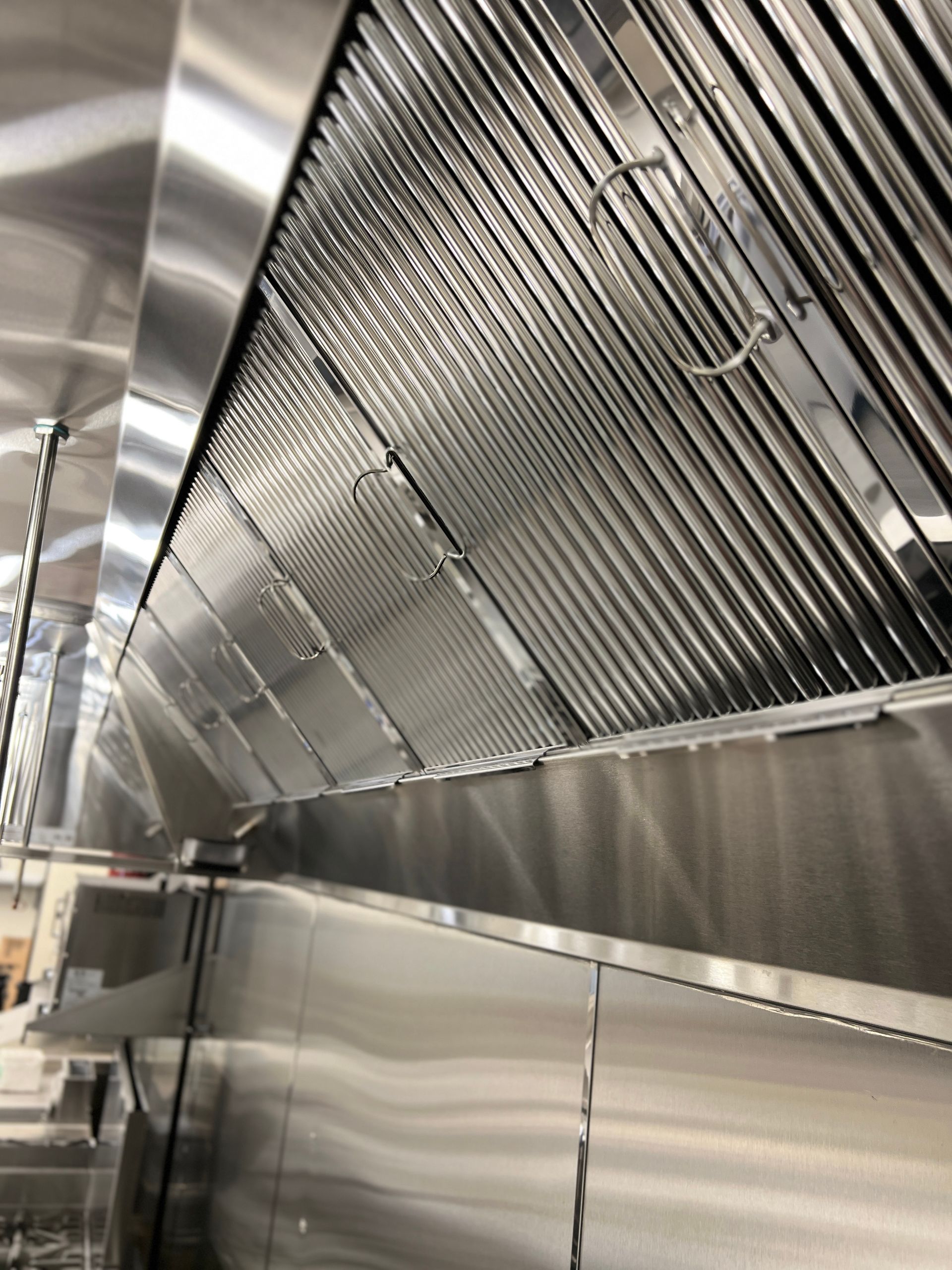 Stainless steel commercial kitchen ventilation hood with metal panels and hanging hooks