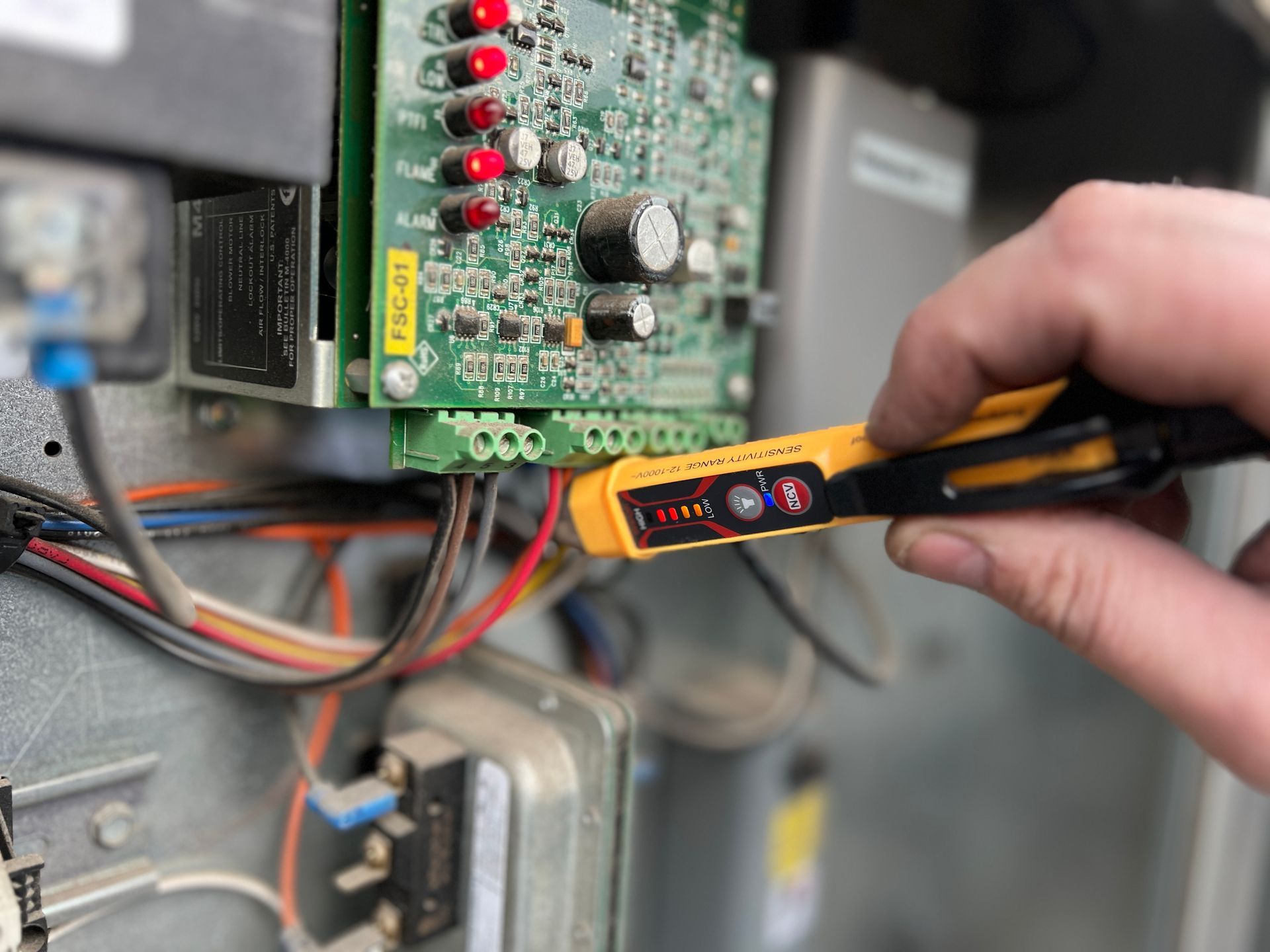 Hand holding a multimeter probe near an electrical circuit board inside equipment panel