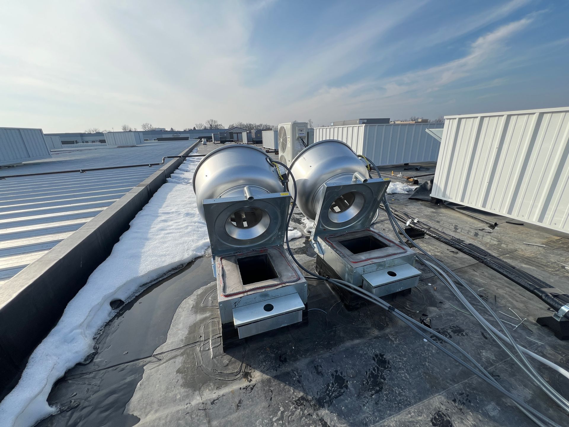 Two shiny stainless steel tanks on a snowy rooftop beside a metal wall under a bright sky