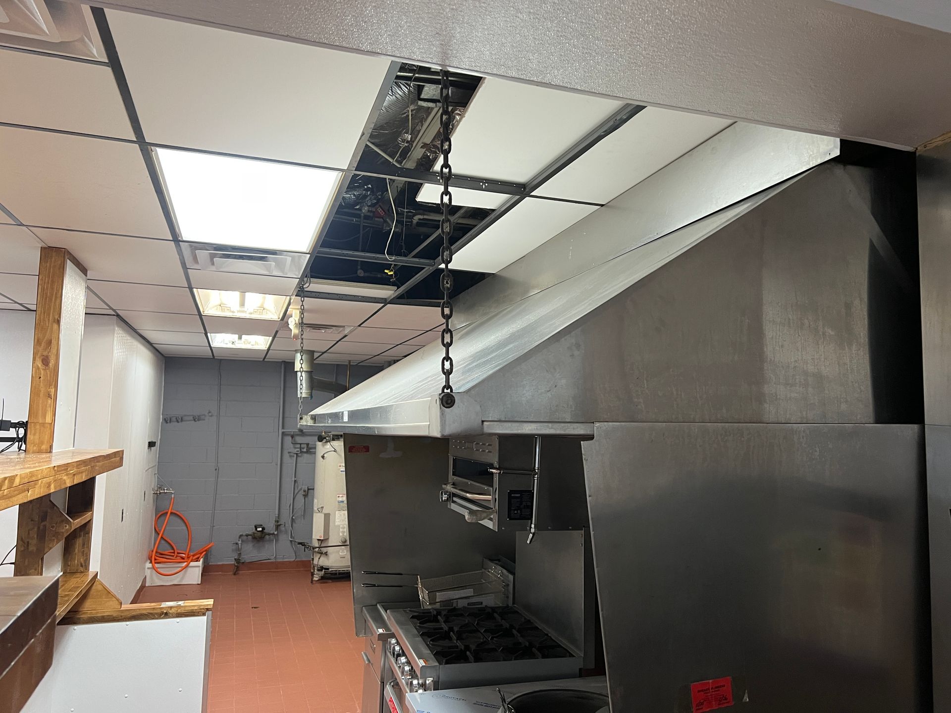 Commercial kitchen with stainless steel equipment and a damaged, open ceiling exposing insulation and wiring