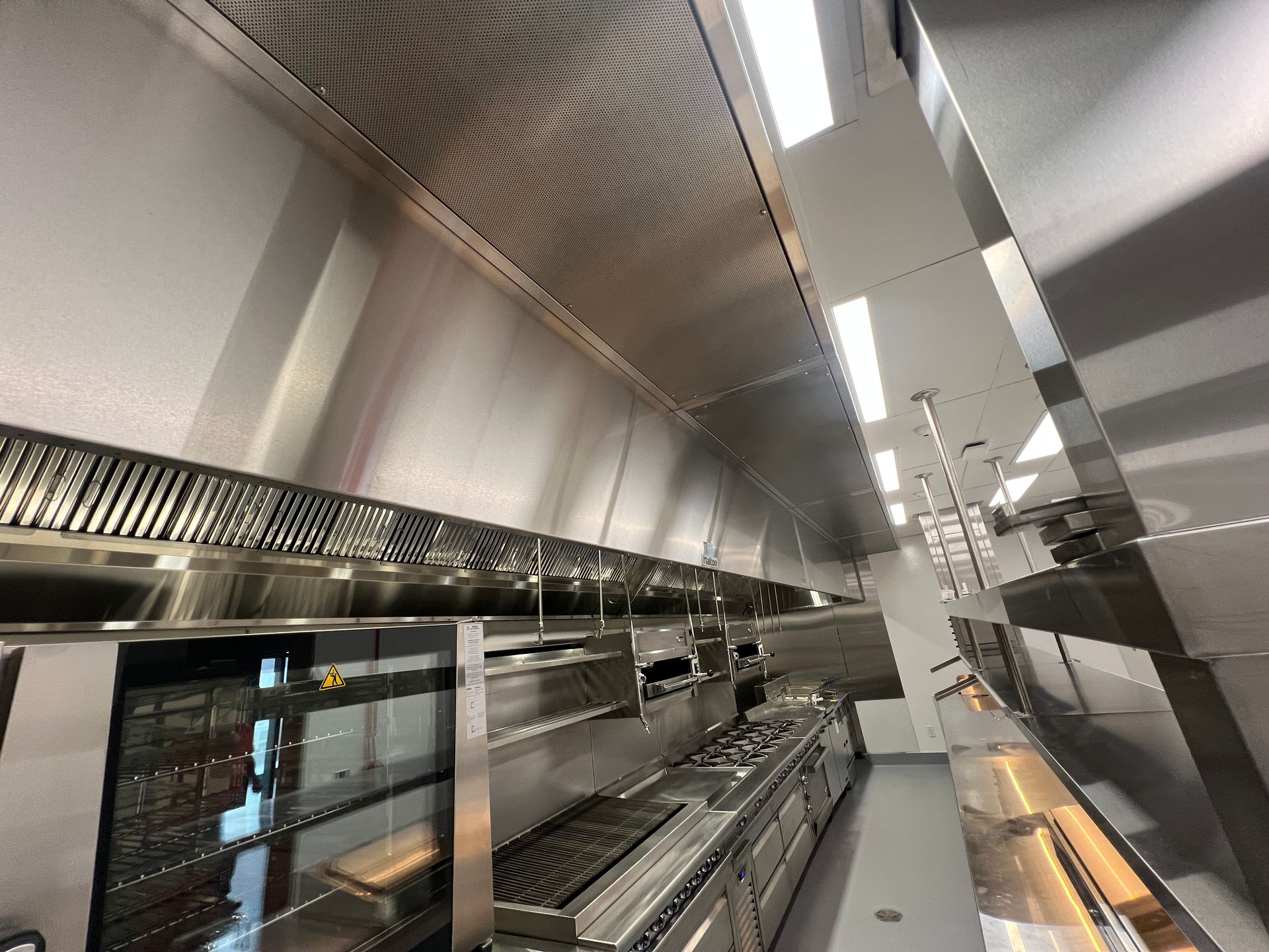 Industrial kitchen with stainless steel counters, vents, and bright overhead lights