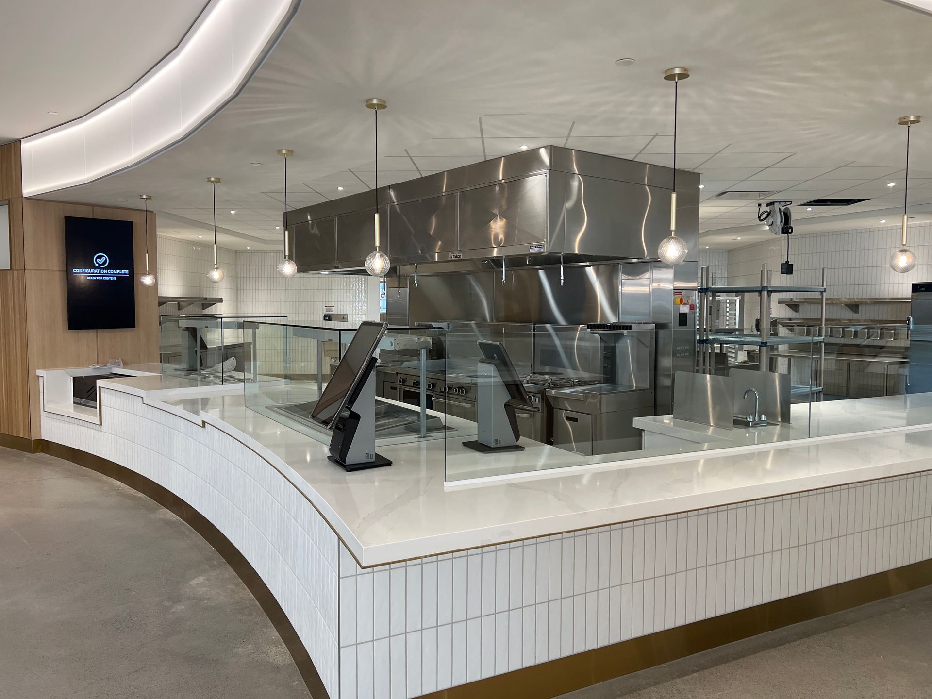 A clean, modern commercial kitchen counter with white tiled base, marble top, point-of-sale kiosks, and stainless steel.