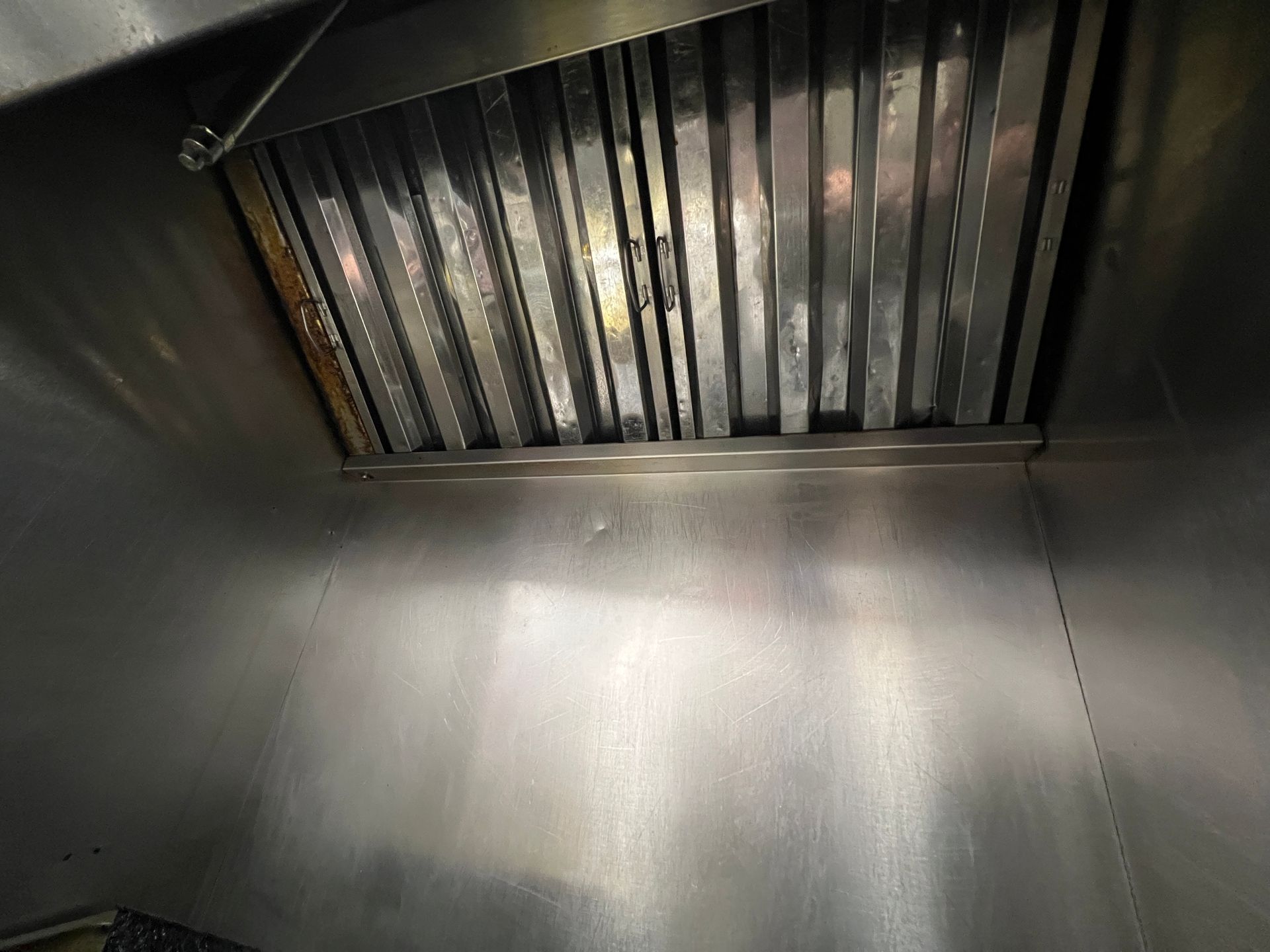 Close-up of a stainless steel kitchen exhaust hood with a metal baffle filter inside.