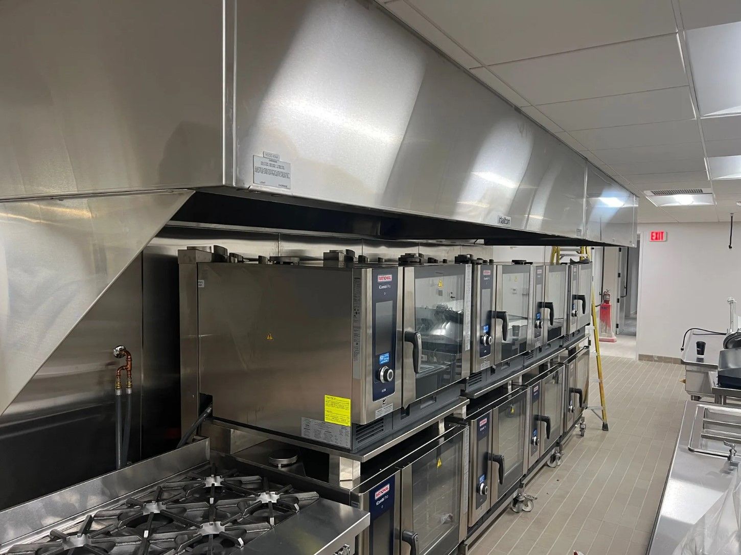 Commercial kitchen with stainless steel hood and ovens. A gas stove is in the foreground.