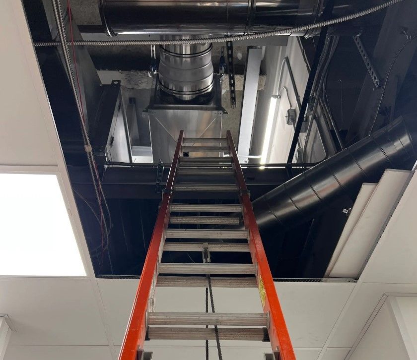 A metal ladder reaching up into a dark ceiling cavity with ductwork and machinery visible.