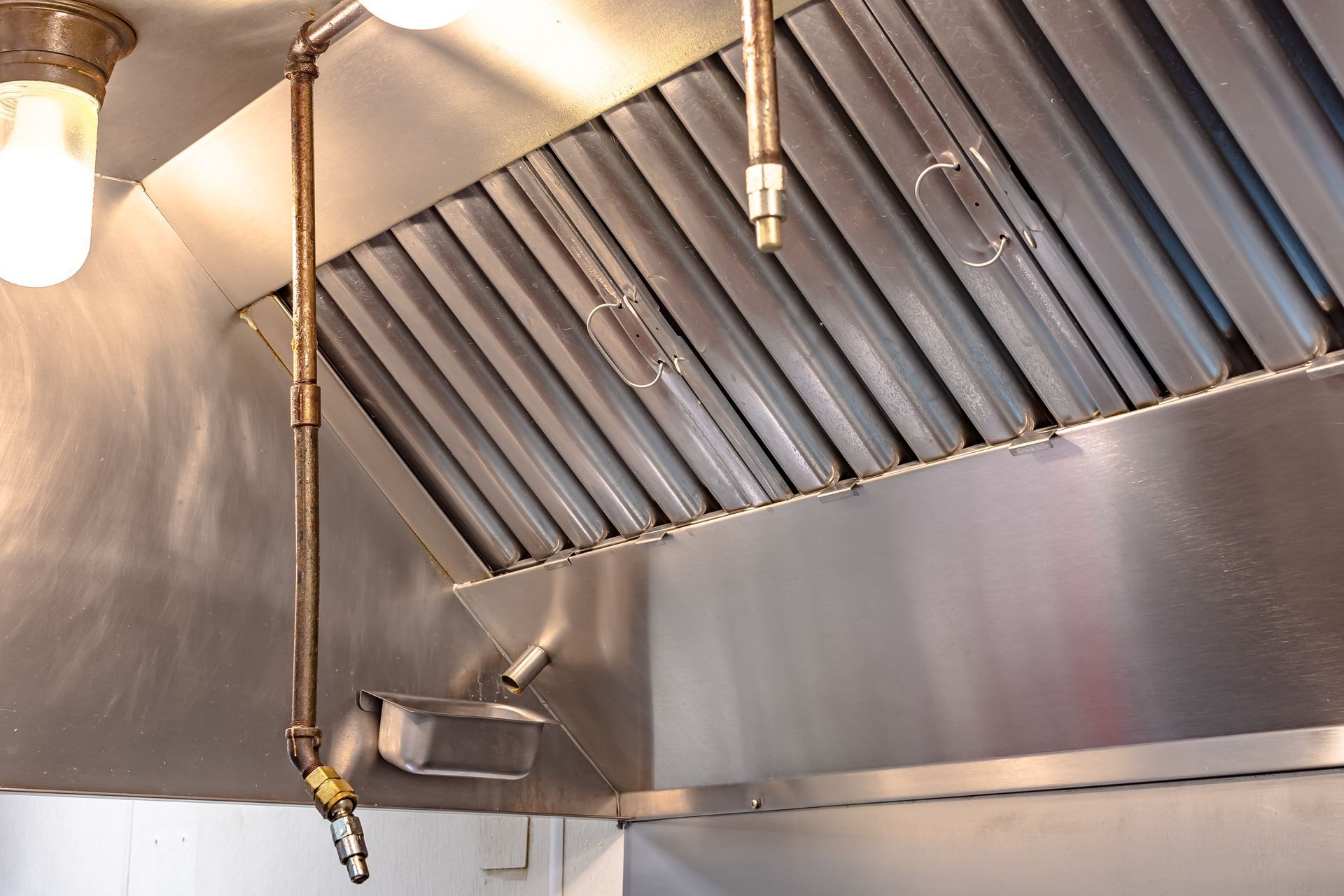 Stainless steel commercial kitchen exhaust hood with vents and hanging fire suppression system