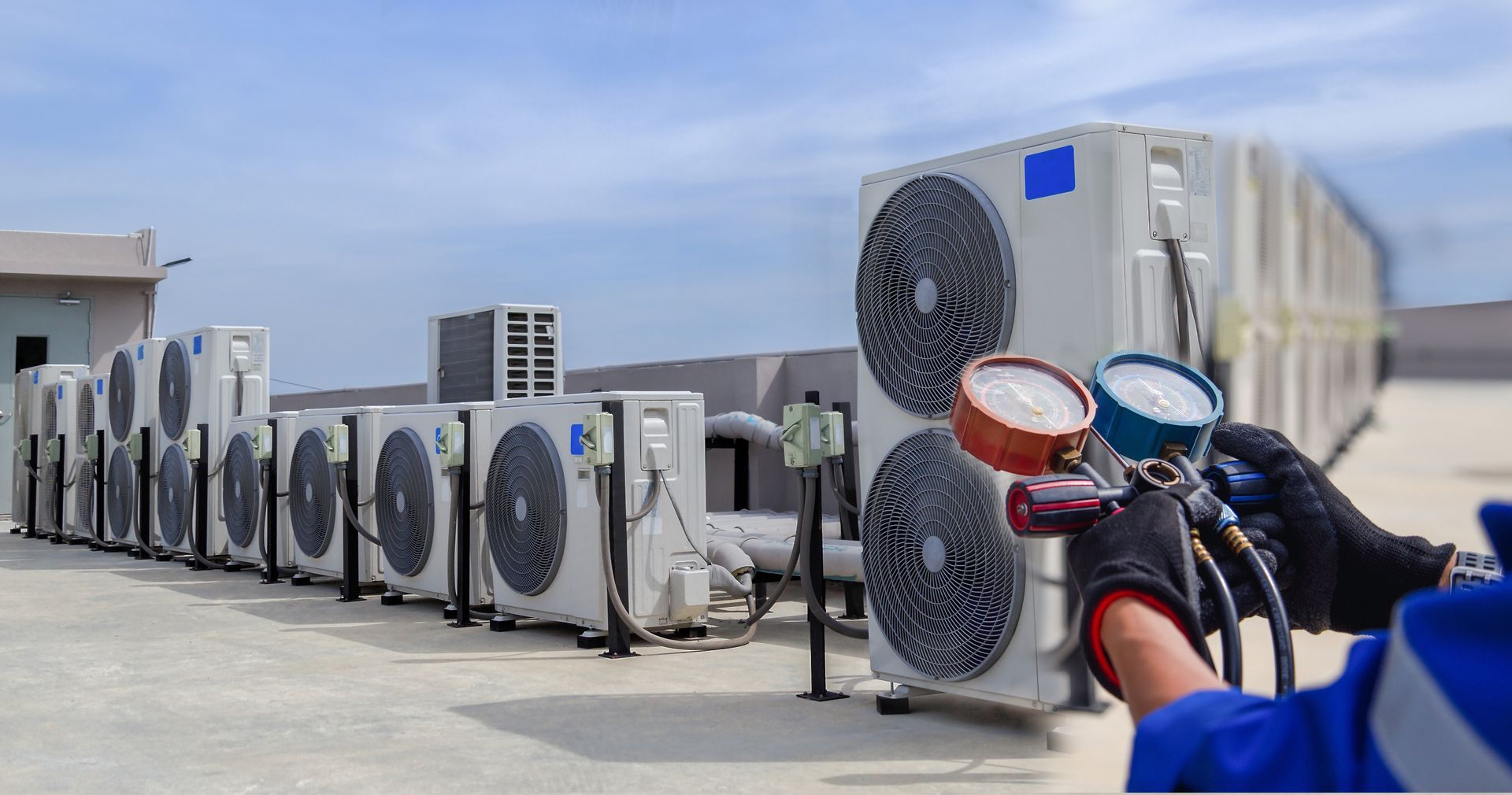 HVAC technician servicing multiple air conditioning units on a rooftop. Gauges visible.