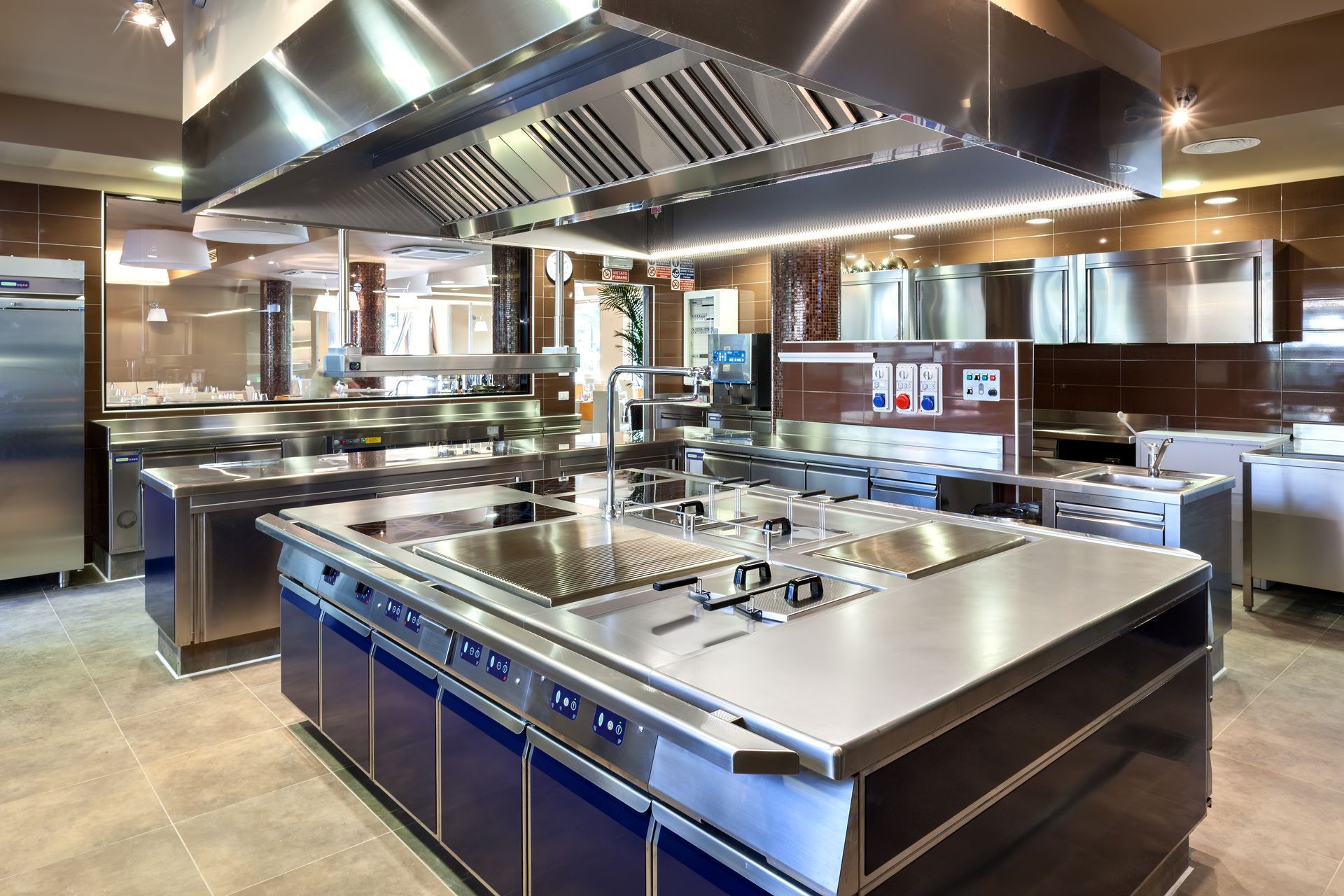 Modern stainless-steel commercial kitchen with large cooking island and overhead ventilation hood