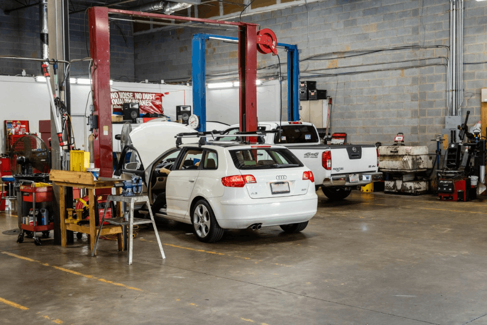 Vehicle inspection, image of a white Audi wagon with its hood open inside a repair shop.