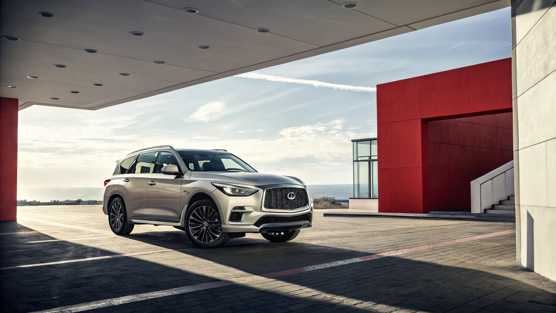 A sleek silver SUV is parked under a modern canopy with a bold red accent wall.