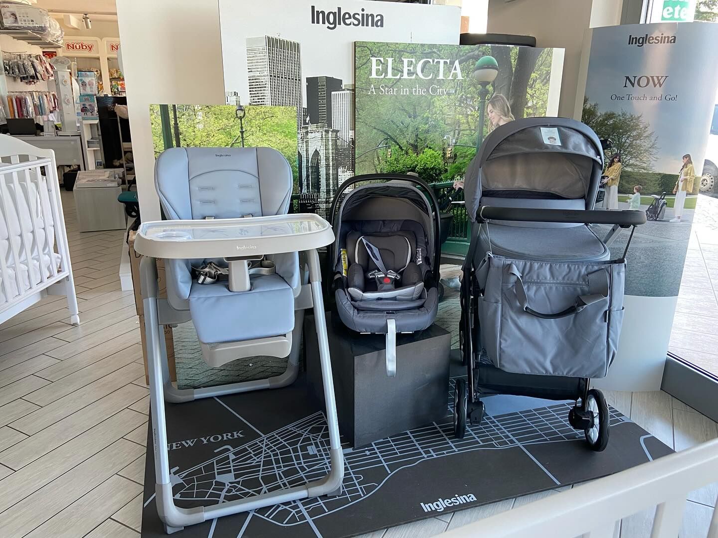 Esposizione di passeggini con seggiolone, seggiolino auto per neonati e passeggino in un'area espositiva.
