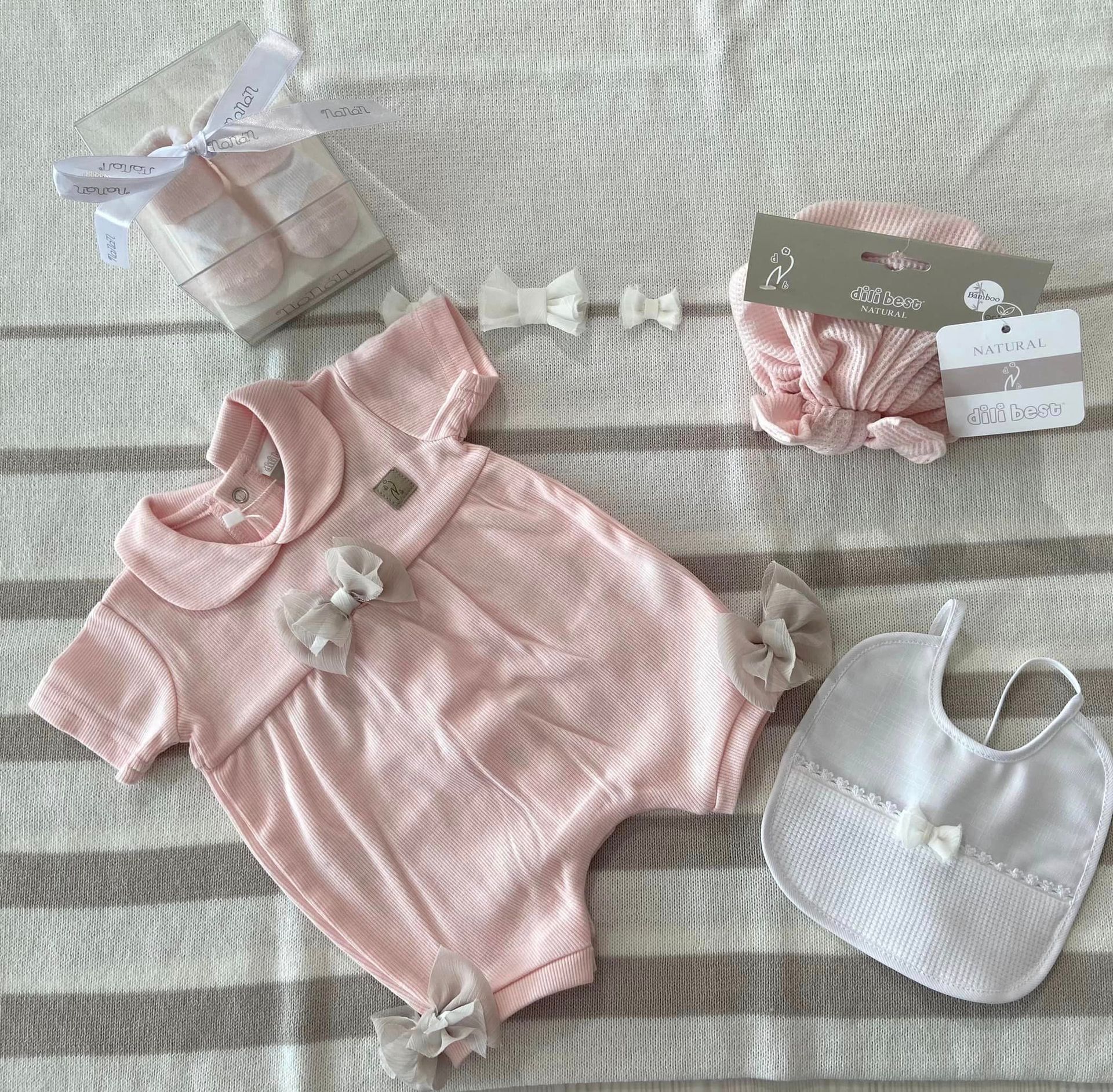 Tutina rosa da neonato con fascia per capelli, calzini e bavaglino bianco abbinati, adagiata su una coperta.