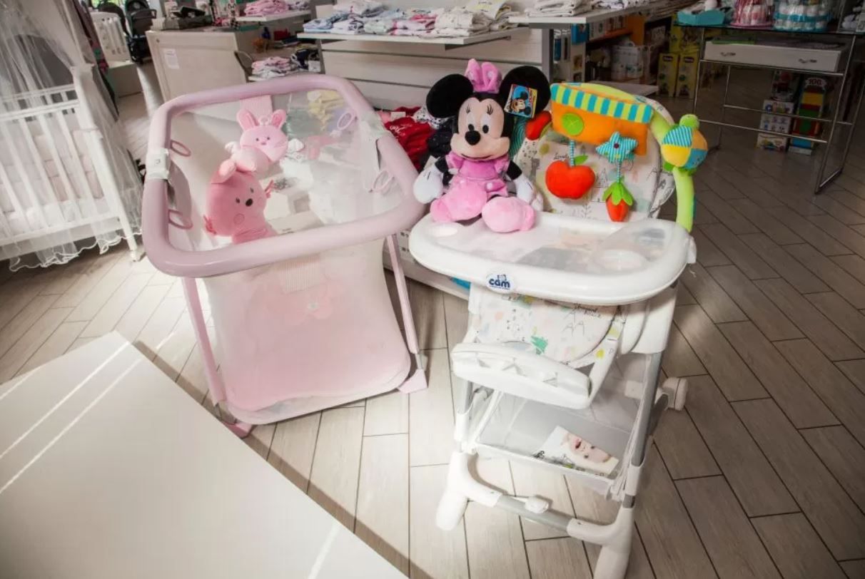 Culla rosa e seggiolone con peluche in un corridoio di un negozio.