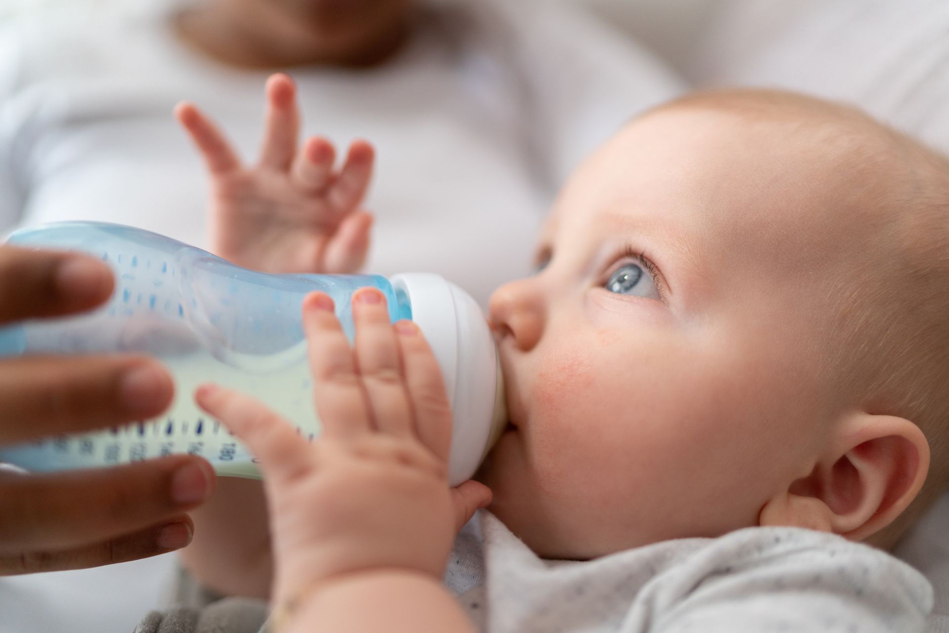 Un bambino che beve da un biberon tenuto dalla mano di un adulto in una scena delicata e ravvicinata.
