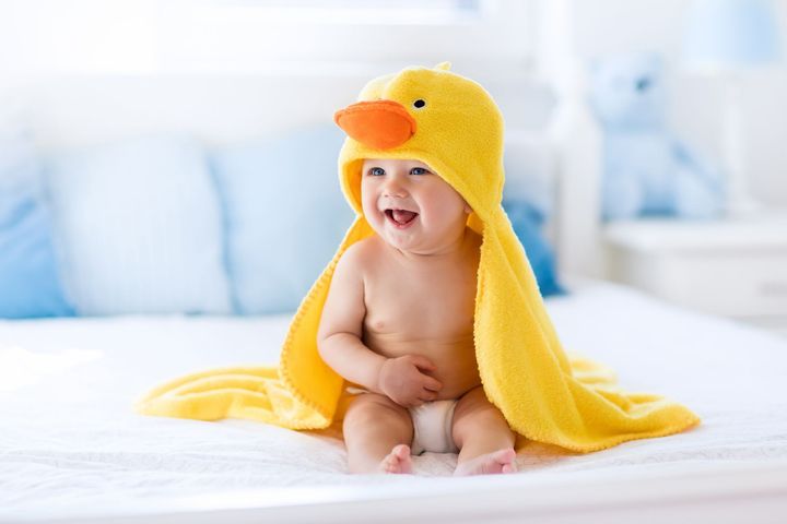 Bambino vestito da papera gialla seduto su un letto e sorridente