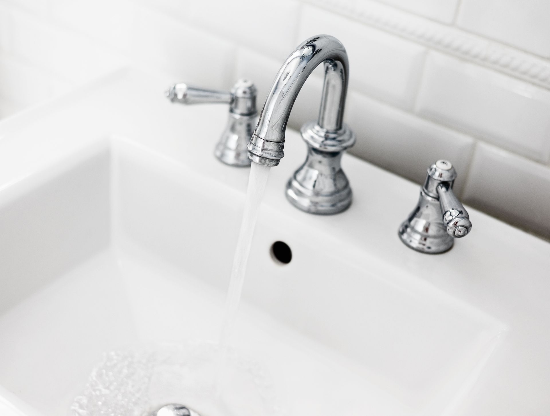 White bathroom sink with chrome faucet, water running.
