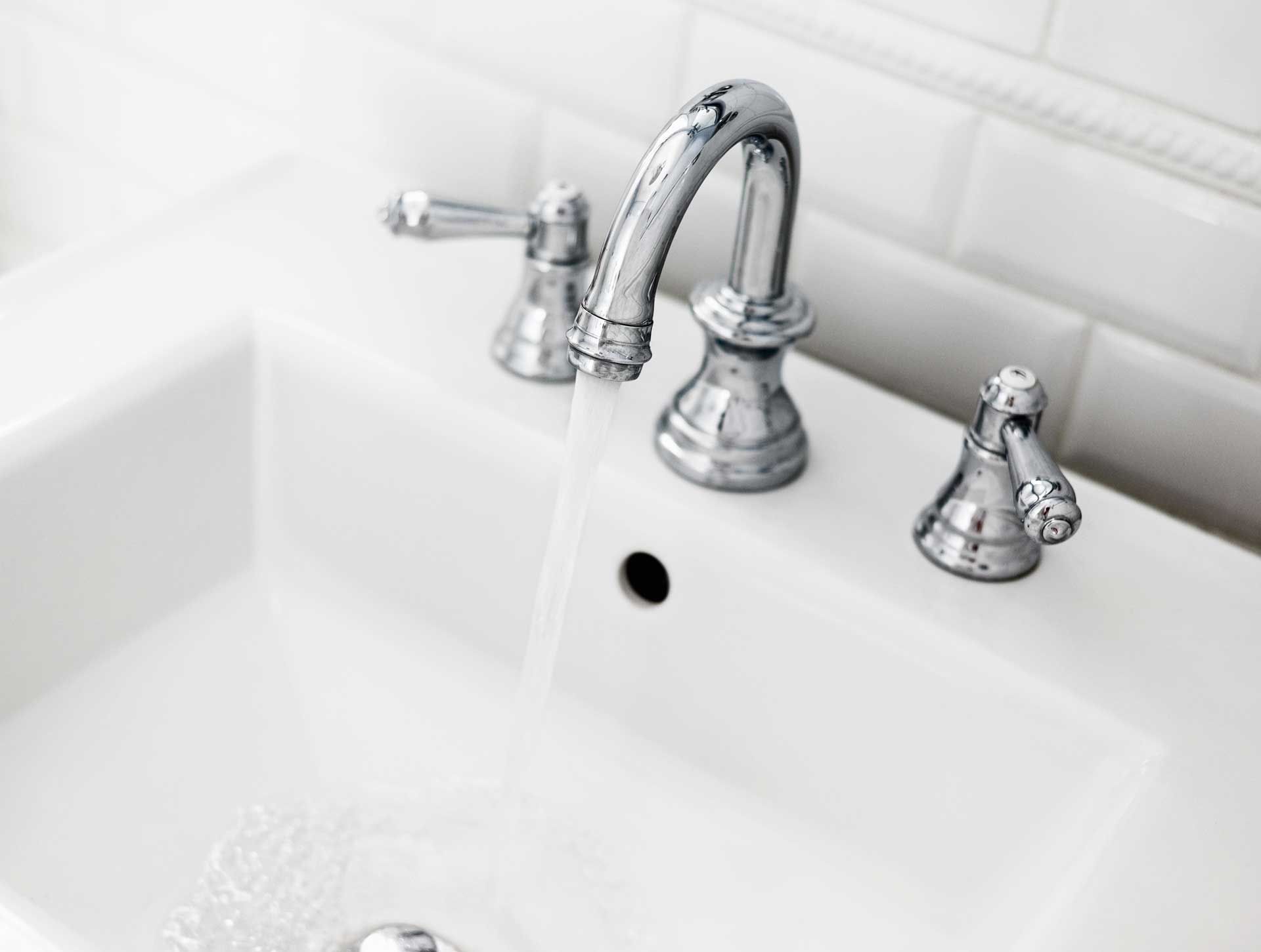 White bathroom sink with chrome faucet, water running.
