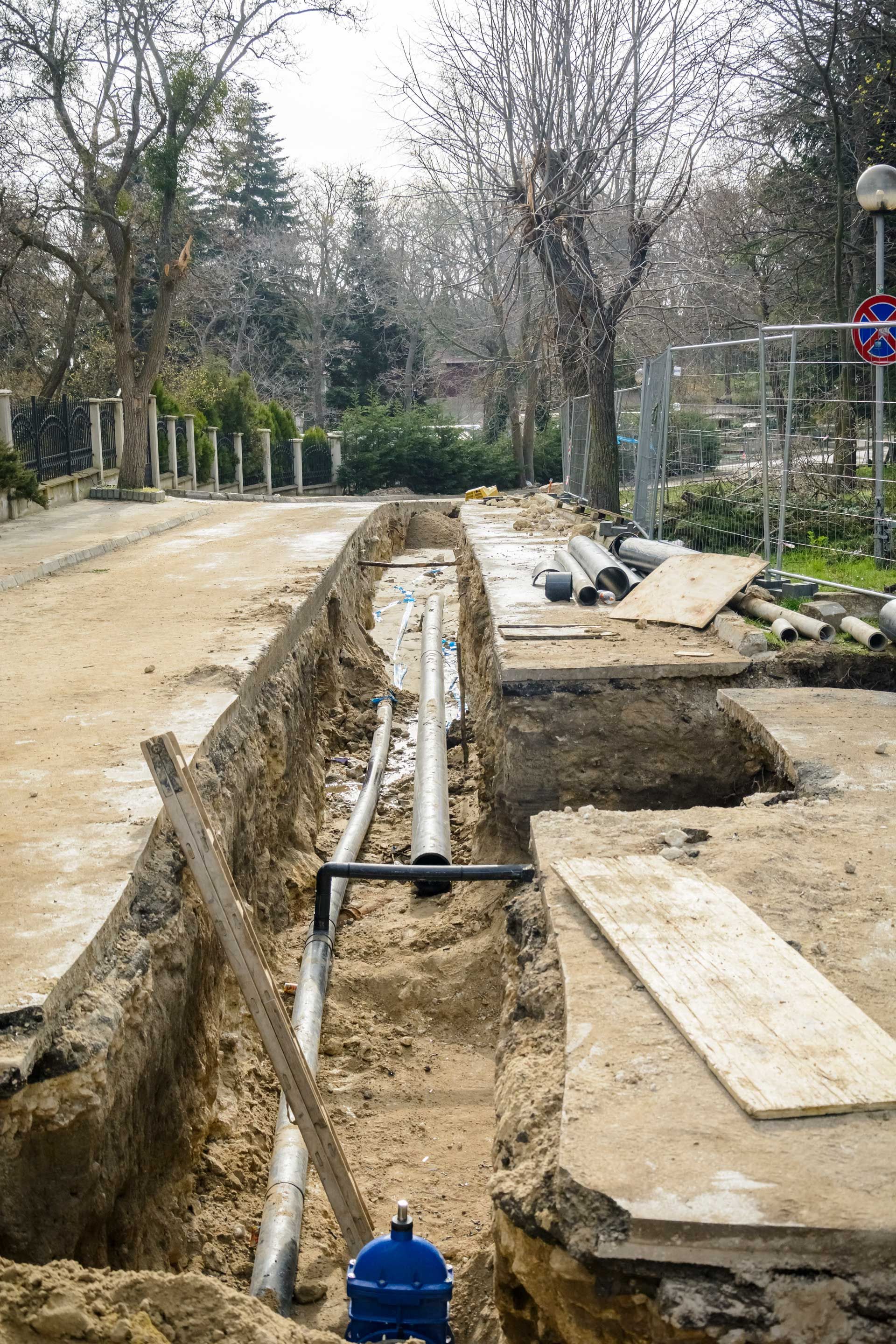 Trench dug with pipes and equipment for construction work. A blue valve is visible.