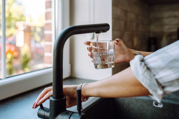 Person filling a glass with water from a black faucet in a kitchen.