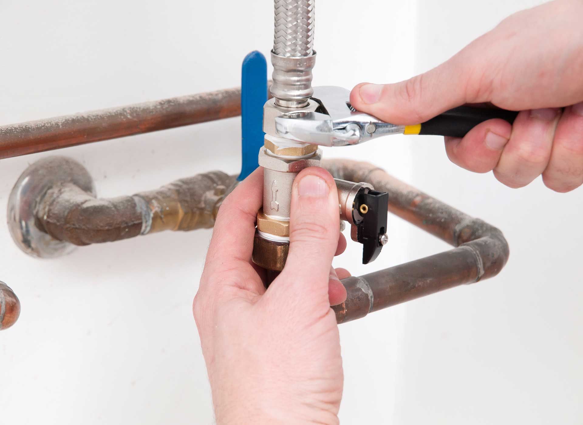 Hands tightening a fitting on copper pipes with a wrench, likely plumbing repair.