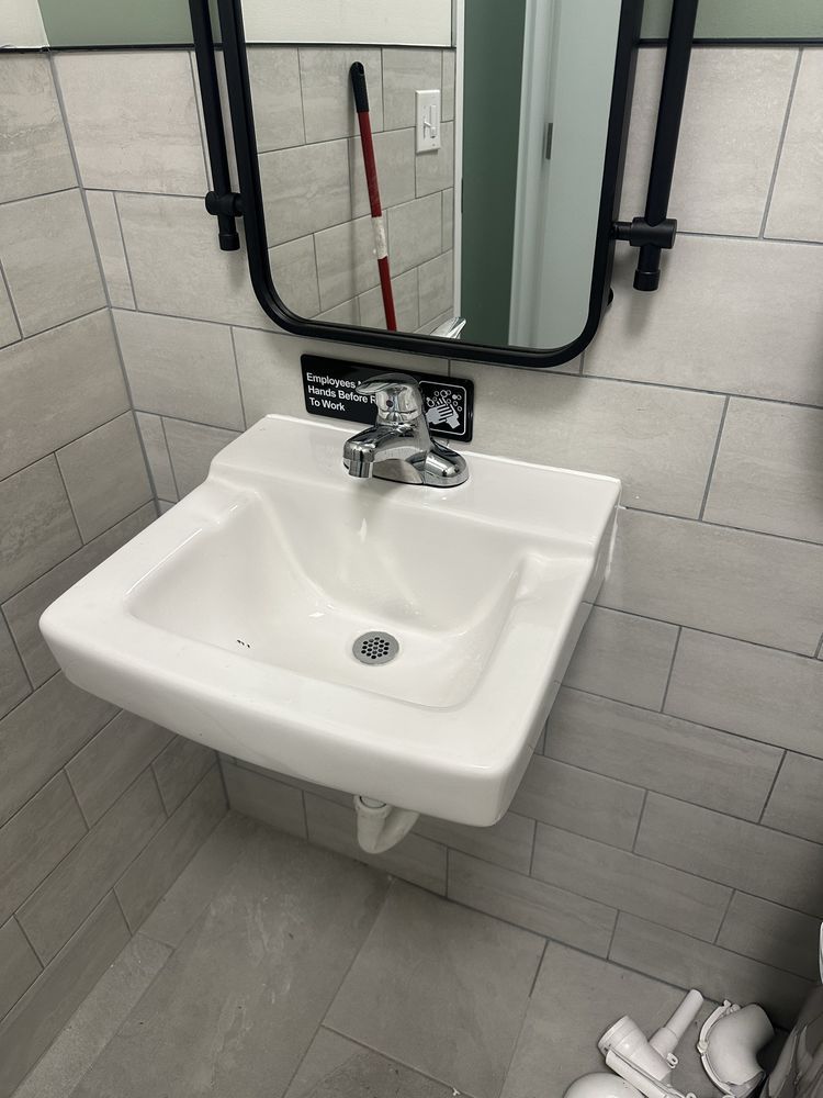 White sink with chrome faucet, mirror above. Gray tiled wall and floor. White sink with chrome faucet, mirror above. Gray tiled wall and floor.